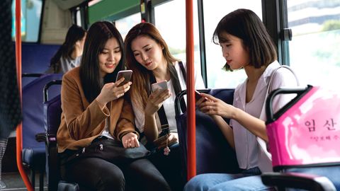 Drei weibliche Teenager sitzen in Seoul im Bus und jeder guckt auf sein Handy
