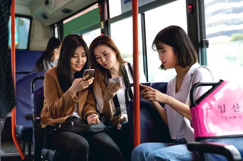 Drei weibliche Teenager sitzen in Seoul im Bus und jeder guckt auf sein Handy