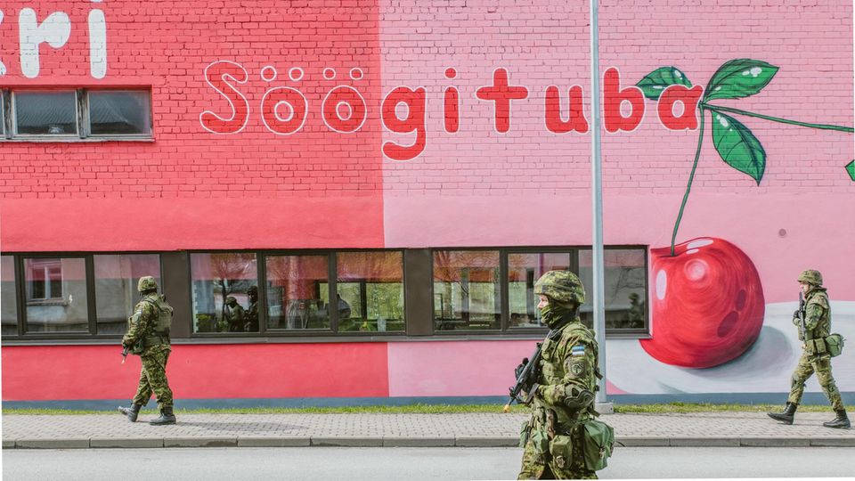 Estnische Selbstverteidigungsgruppen Kaitseliit (Tartu Unit) gehen an einer Kantine in Tammsalu, Estland, (darf das genannt werden?) vorbei während der Übung Kevadtorm, bei der sie mit estnischem und ausländischem Militär gemeinsam trainieren. Ein Teil der Selbstverteidigungsgruppe vor einer, in Rosa gehaltenen, Kantine