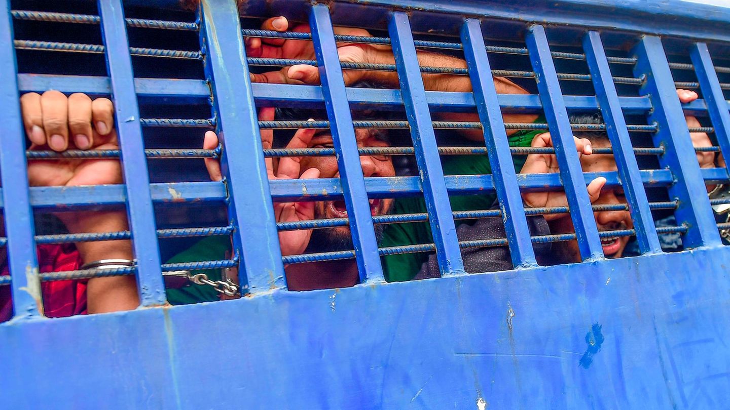 Durch die blauen Gitter eines Gefangenentransporters ist das verzweifelt Gesicht eines Mannes zu sehen