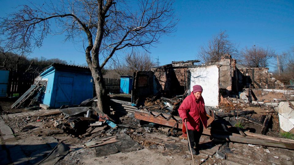 Eine alte Frau vor einem zerstörten Haus in der Ostukraine