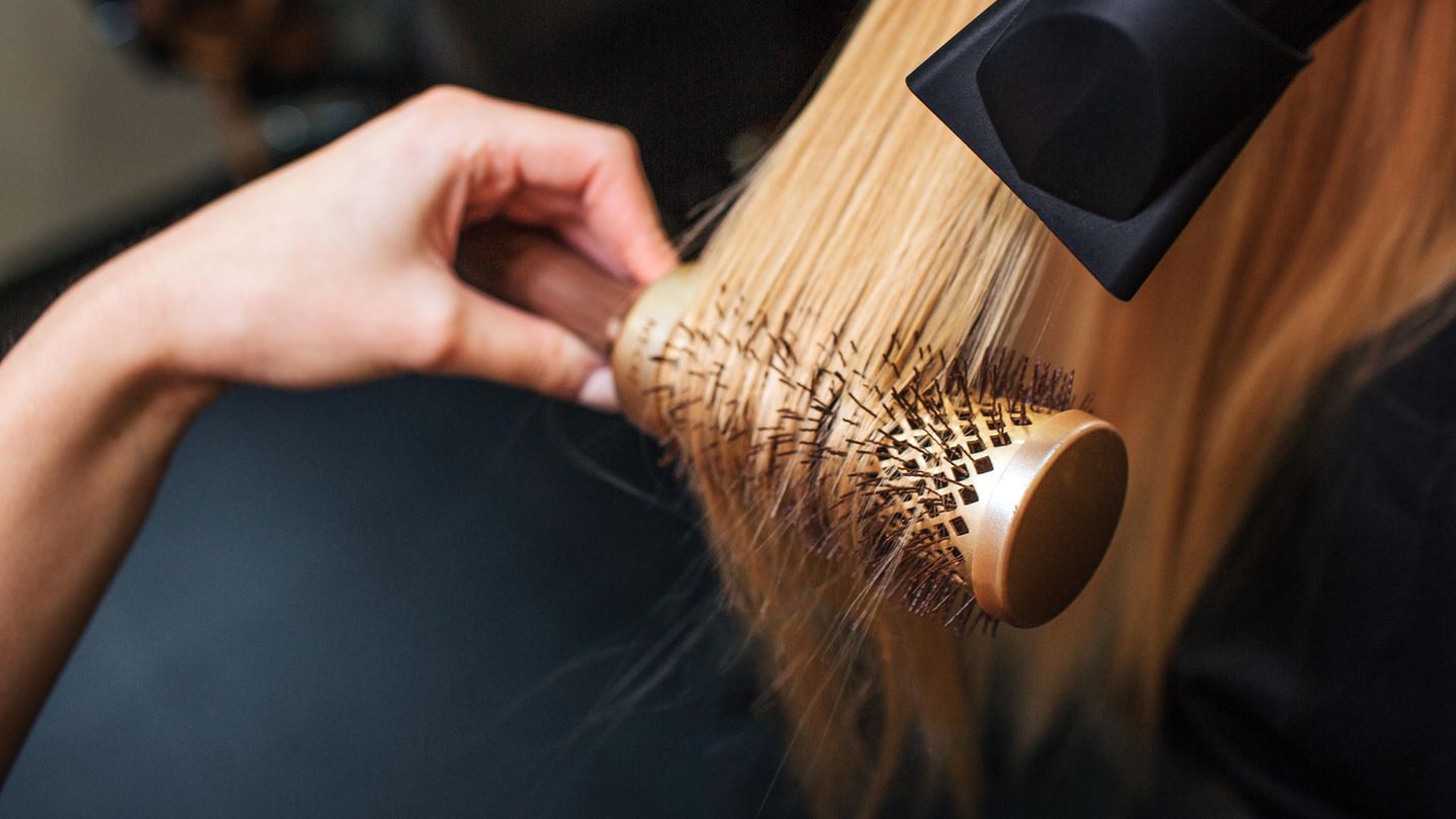 Eine Friseurin trocknet das Haar einer Kundin über einer Rundbürste mit dem Fön