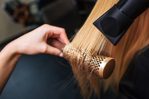 Eine Friseurin trocknet das Haar einer Kundin über einer Rundbürste mit dem Fön