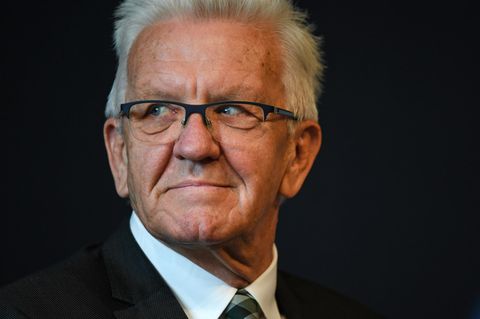 Ein Mann mit weißem Igelschnitt und schwarzem, eckigen Brille schaut mit nach rechts gedrehtem Kopf aus den Augenwinkeln