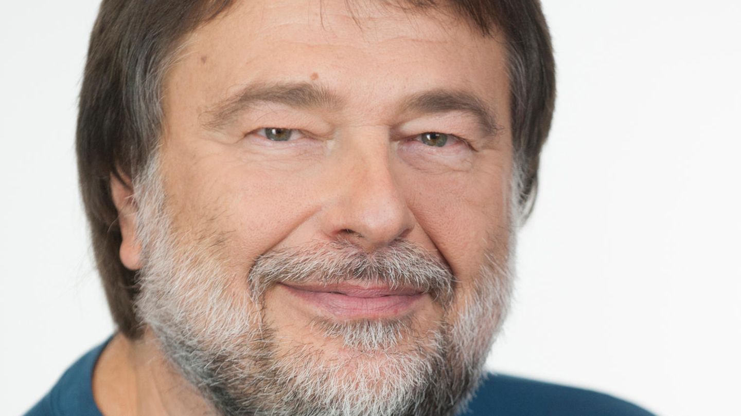 Ein Mann mit braunem Seitenscheitel und grau-weißem Vollbart lächelt in die Kamera