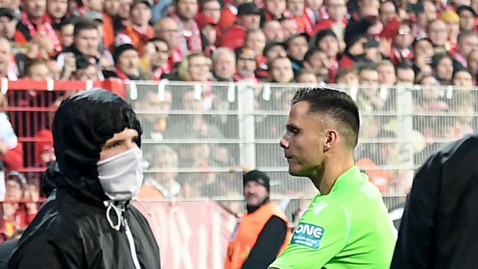 Torwart Rafael Gikiewicz steht in hellgrünem Torwart-Dress Vermummten in schwarzen Jacken gegenüber