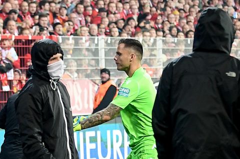 Torwart Rafael Gikiewicz steht in hellgrünem Torwart-Dress Vermummten in schwarzen Jacken gegenüber