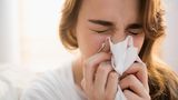 Erkältung: Eine Frau niest in ein Taschentuch