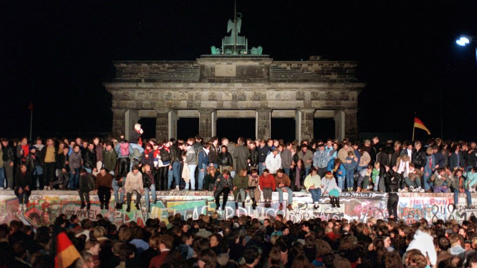 Feiernde Ost- und Westdeutsche auf der Berliner Mauer am Brandenburger Tor in der Nacht des 9. November 1989
