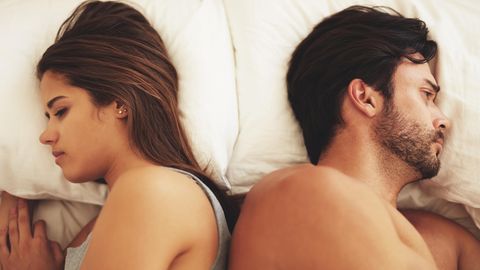 Frau und Mann schauen liegen mit dem Rücken zueinander gekehrt im Bett
