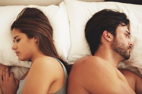Frau und Mann schauen liegen mit dem Rücken zueinander gekehrt im Bett