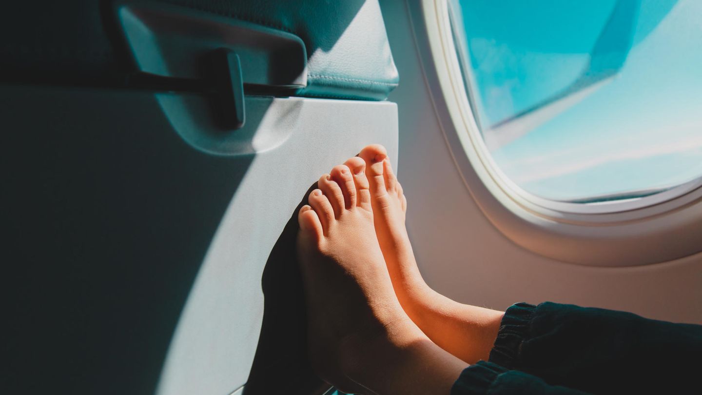 Ein Kind sitzt im Flugzeug und hat die nackten Füße gegen den Vordersitz gepresst