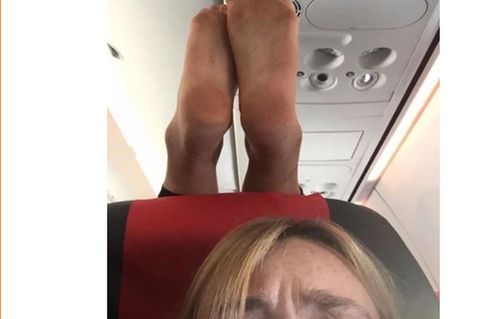 Ein Selfie zeigt eine Frau im Flugzeug, hinter hier die nackten Füße ihres Sitznachbarn