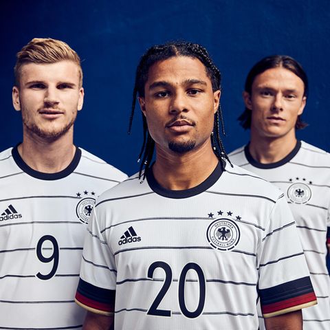 Timo Werner, Serge Gnabry und Nico Schulz stehen vor einem blauen Hintergrund und schauen in weißen Fußball-Trikots geradeaus