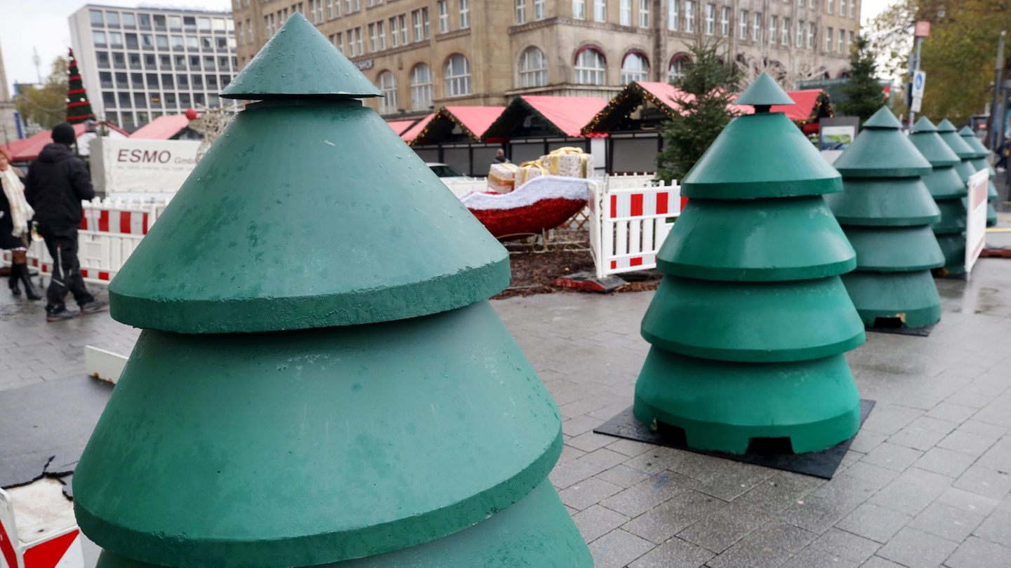 Als Weihnachtsbäume verkleidete Beton-Durchfahrtssperren stehen vor dem Eingangsbereich eines Weihnachtsmarktes