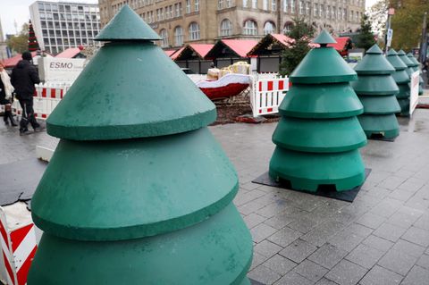 Als Weihnachtsbäume verkleidete Beton-Durchfahrtssperren stehen vor dem Eingangsbereich eines Weihnachtsmarktes