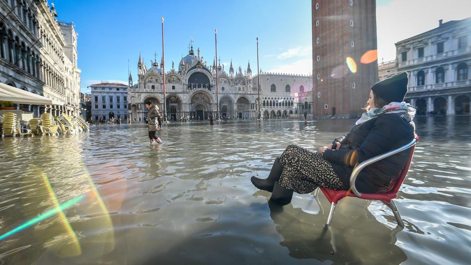 Sie nimmt es mit Galgenhumor: Eine Frau sitzt auf einem Stuhl im Hochwasser auf dem Markusplatz Sie nimmt es mit Galgenhumor: Eine Frau sitzt auf einem Stuhl im Hochwasser auf dem Markusplatz