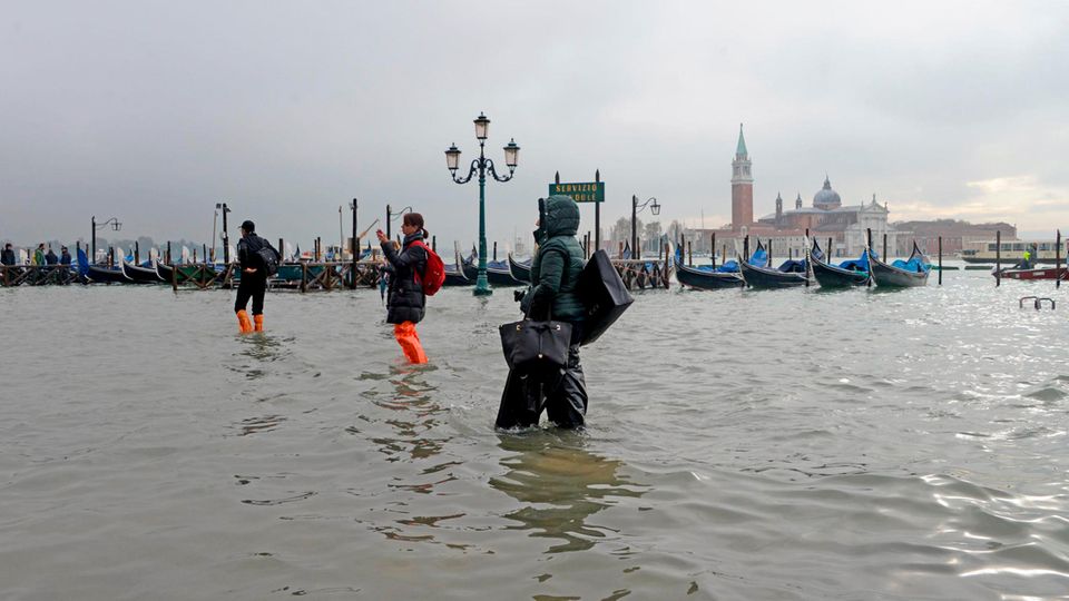 Menschen waten über einen überfluteten Platz in Venedig