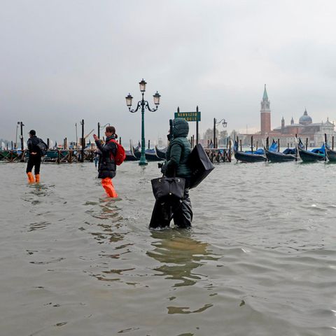 Menschen waten über einen überfluteten Platz in Venedig