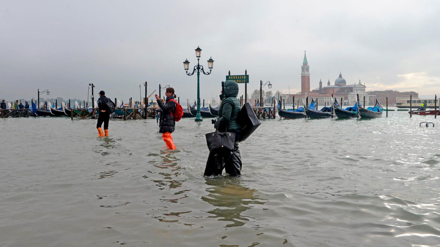 Menschen waten über einen überfluteten Platz in Venedig