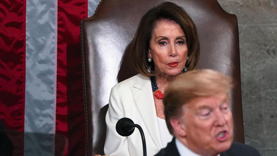 Pelosi, auf einem großen Sessel sitzend, beäugt den vor ihr stehenden Trump
