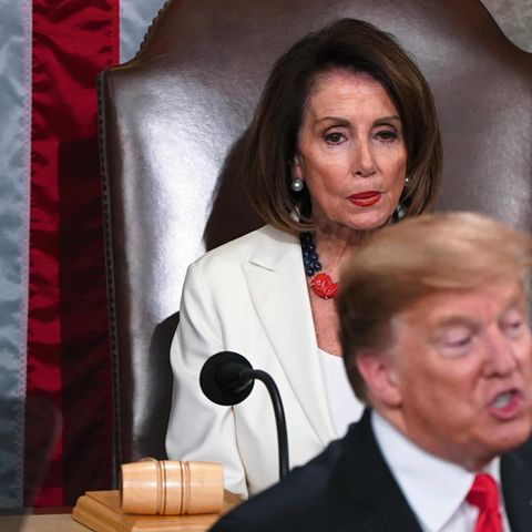 Pelosi, auf einem großen Sessel sitzend, beäugt den vor ihr stehenden Trump