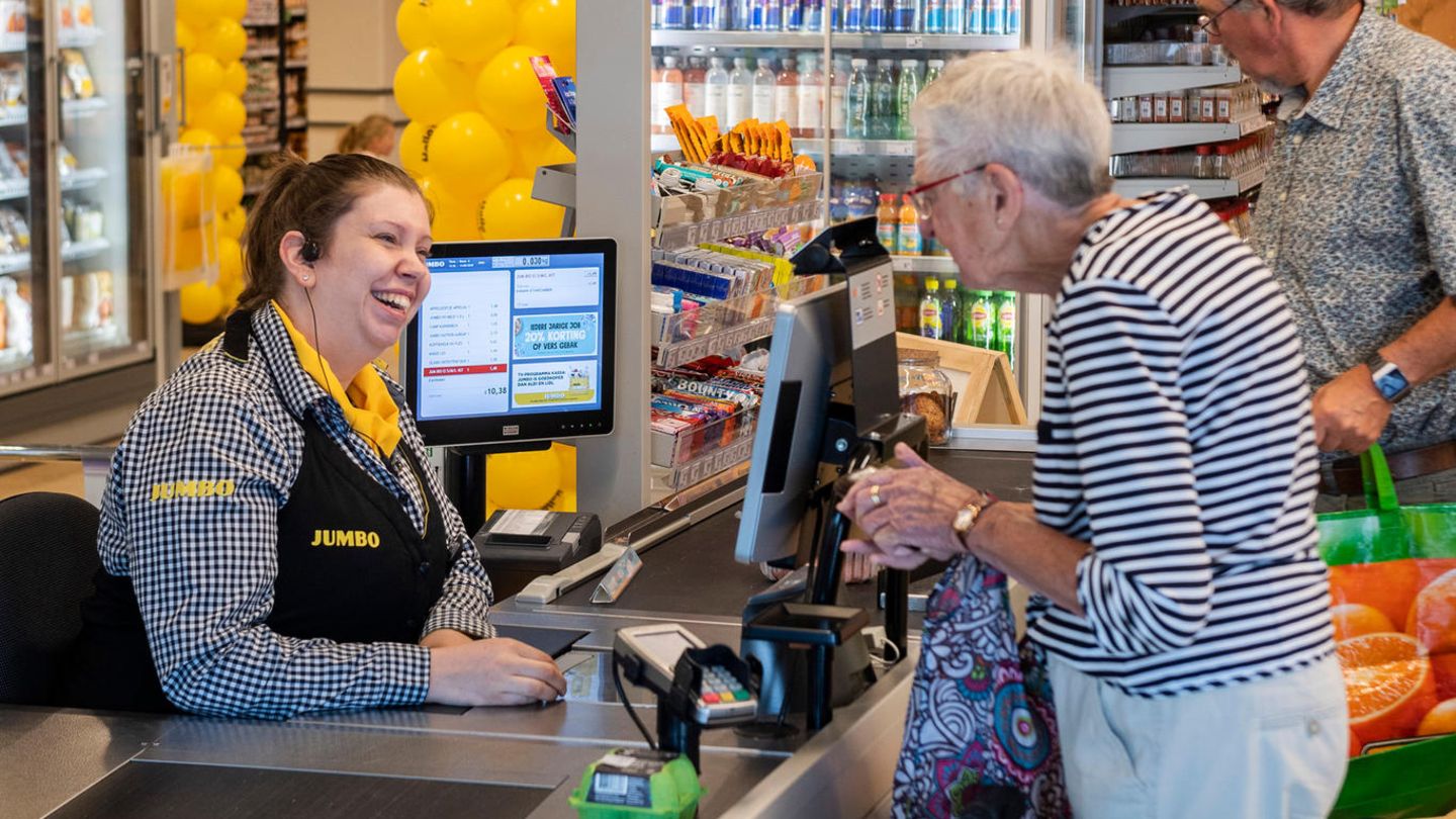 Eine alte Damme steht an einer Supermarktkasse und unterhält sich mit der Kassiererin