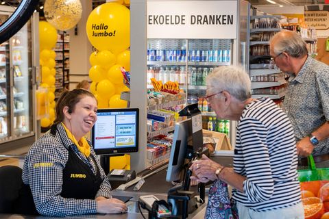 Eine alte Damme steht an einer Supermarktkasse und unterhält sich mit der Kassiererin