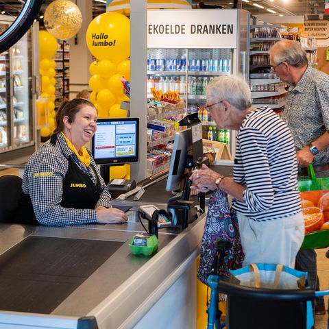Eine alte Damme steht an einer Supermarktkasse und unterhält sich mit der Kassiererin