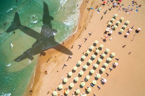 Der Schatten eines Flugzeugs über Meer und Strand