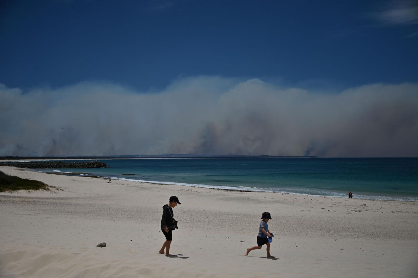 Sorgloser Spaß vor bedrohlicher Kulisse: Während diese Kinder am Strand von Forster, 300 Kilometer nördlich von Sydney, im Sand spielen, wüten im Hintergrund gewaltige Buschfeuer.
