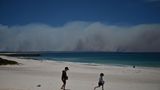 Sorgloser Spaß vor bedrohlicher Kulisse: Während diese Kinder am Strand von Forster, 300 Kilometer nördlich von Sydney, im Sand spielen, wüten im Hintergrund gewaltige Buschfeuer.