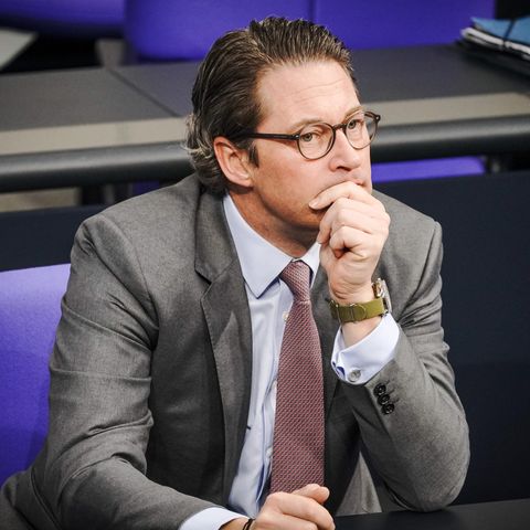 Bundesverkehrsminister Andreas Scheuer sitzt im Bundestag und stützt seinen Kopf auf die linke Hand. Er trägt Anzug und Krawatte