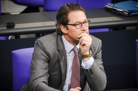 Bundesverkehrsminister Andreas Scheuer sitzt im Bundestag und stützt seinen Kopf auf die linke Hand. Er trägt Anzug und Krawatte