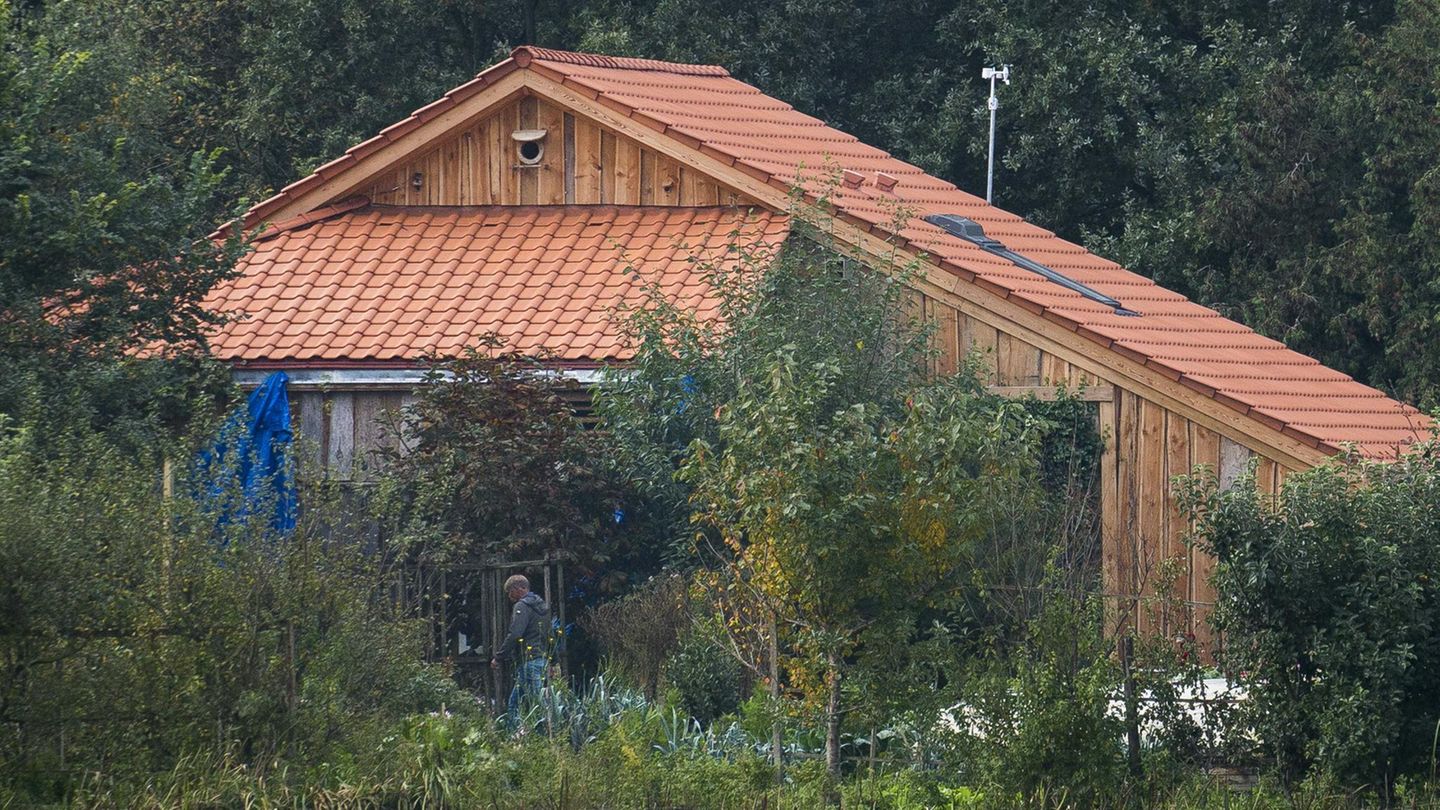 Ein Gebäude mit rotem Ziegeldach und hölzerner Verschalung ist hinter Büschen zu sehen
