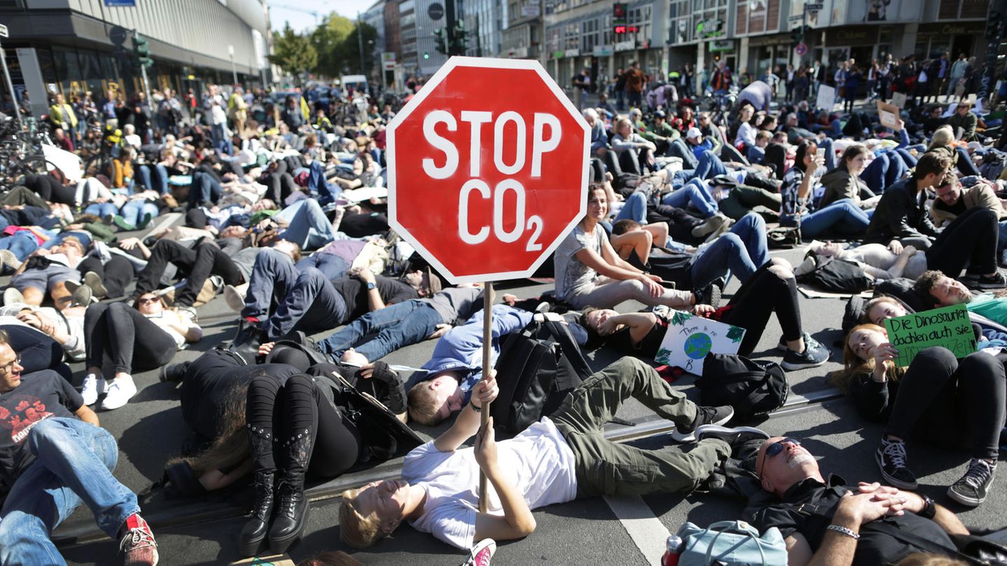 Auf einer Kreuzung in Düsseldorf liegen lauter Demonstranten. Einer hält ein Stoppschild mit mit "Stop CO2" hoch