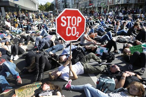 Auf einer Kreuzung in Düsseldorf liegen lauter Demonstranten. Einer hält ein Stoppschild mit mit "Stop CO2" hoch