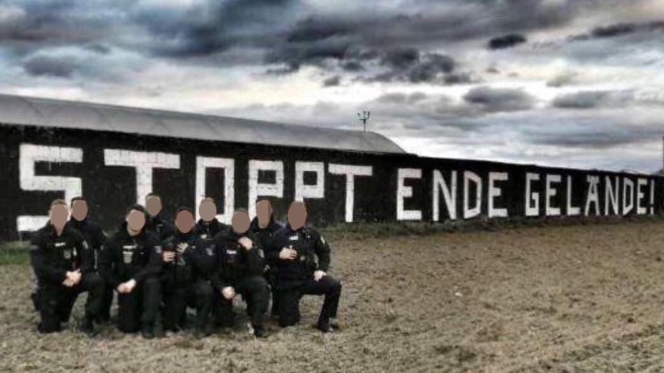 Neun Polizisten in Uniform knien auf einem Knie vor einem "Stoppt Ende Gelände!"-Graffito