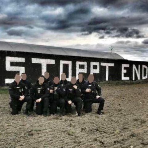 Neun Polizisten in Uniform knien auf einem Knie vor einem "Stoppt Ende Gelände!"-Graffito