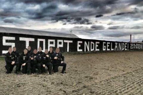 Neun Polizisten in Uniform knien auf einem Knie vor einem "Stoppt Ende Gelände!"-Graffito