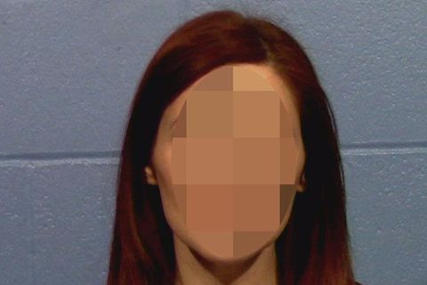 Eine Frau mit rotbraunen, halblangen Haaren sitzt in violettem Oberteil vor einer grauen Mauer und schaut direkt in die Kamera
