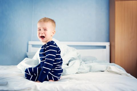 Ein Junge hockt weinend auf einem Bett