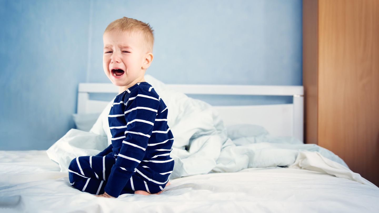 Ein Junge hockt weinend auf einem Bett
