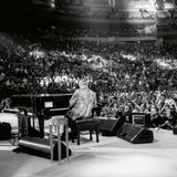 Elton John von sitzt mit dem Rücken zur Kamera vor Publikum am Flügel