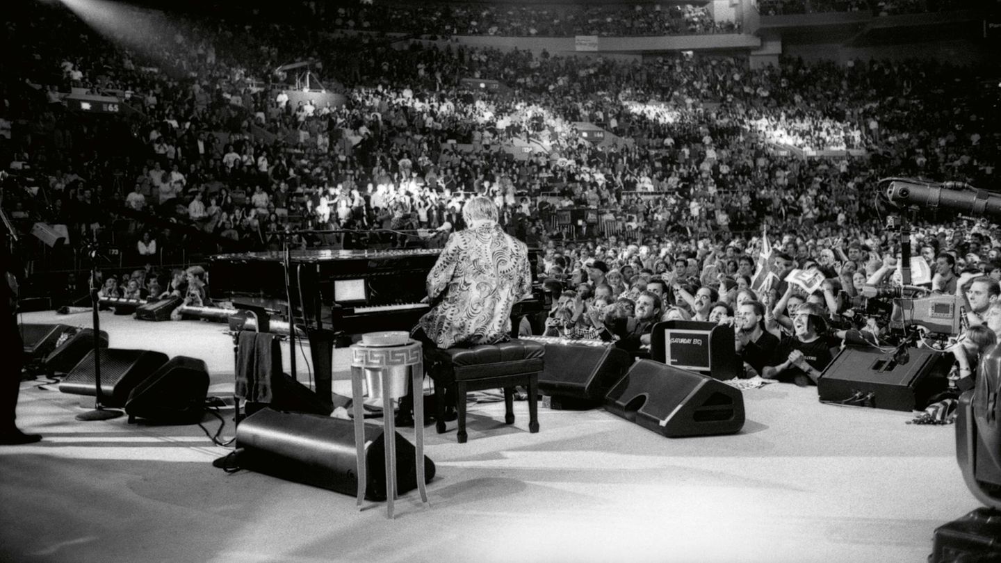 Elton John von sitzt mit dem Rücken zur Kamera vor Publikum am Flügel