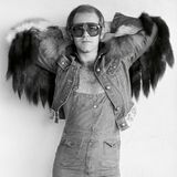 Elton John in Latzhose und Jeansjacke mit Fell