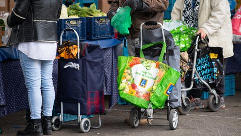 Gäste der Münchner Tafel stehen mit Plastiktüten an der Ausgabestelle