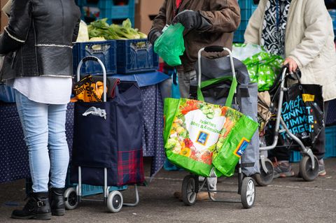 Gäste der Münchner Tafel stehen mit Plastiktüten an der Ausgabestelle