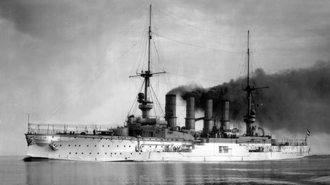 Ein schwarz-weiß-Foto zeigt ein Kriegsschiff mit vier stark rauchenden Schornsteinen