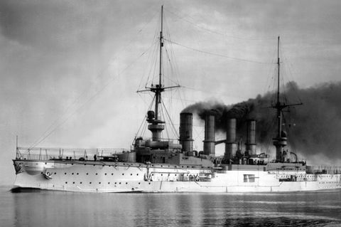 Ein schwarz-weiß-Foto zeigt ein Kriegsschiff mit vier stark rauchenden Schornsteinen